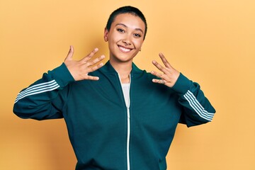 Wall Mural - Beautiful hispanic woman with short hair wearing sporty jacket showing and pointing up with fingers number nine while smiling confident and happy.