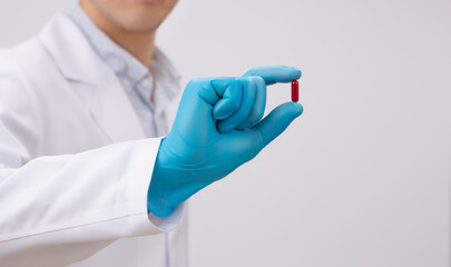 Doctor hand holding medical red capsule pill between fingers against white background - 의사가 의료용 파란색 장갑을 끼고 빨간색 알약 캡슐을 손으로 들고 있는 모습