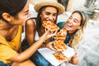 © Davide Angelini - Three young female friends sitting outdoor and eating pizza - Happy women having fun enjoying a day out on city street - Happy lifestyle and tourism concept