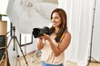 © Krakenimages.com - Young hispanic photographer woman smiling happy using camera at photo studio.