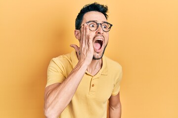 Canvas Print - Young hispanic man wearing casual clothes and glasses shouting and screaming loud to side with hand on mouth. communication concept.