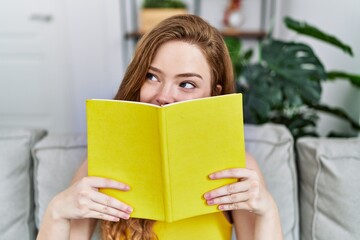 Canvas Print - Young redhead girl smiling happy covering face with book at home