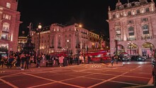 Timelapse Of The Piccadilly Circus In London At Night. People Rushing Through The Streets Of London With Neon Lights Around Them.