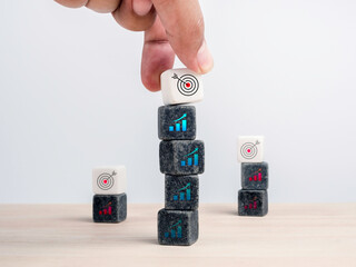 Poster - Target, different business challenge goals concept. Hand put white cube blocks with target icon symbol on black block stacks with chart icon sign on wooden table on white background, minimal style.