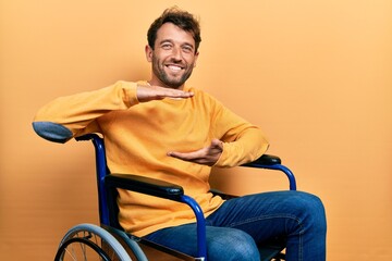 Poster - Handsome man with beard sitting on wheelchair gesturing with hands showing big and large size sign, measure symbol. smiling looking at the camera. measuring concept.