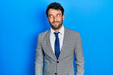 Handsome man with beard wearing business suit and tie smiling looking to the side and staring away thinking.