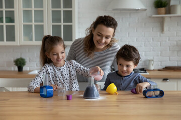 Wall Mural - Happy caring young mother helping little children son daughter making chemical experiments or tests in modern kitchen, improving knowledge, studying together in playful manner, homeschooling concept.