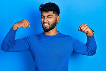 Canvas Print - Arab man with beard wearing casual blue sweater showing arms muscles smiling proud. fitness concept.