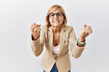 Wall Mural - Middle age blonde business woman standing over isolated background angry and mad raising fists frustrated and furious while shouting with anger. rage and aggressive concept.