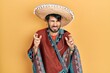 © Krakenimages.com - Young hispanic man holding mexican hat gesturing finger crossed smiling with hope and eyes closed. luck and superstitious concept.