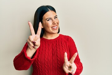 Poster - Beautiful brunette woman wearing wool winter sweater smiling looking to the camera showing fingers doing victory sign. number two.