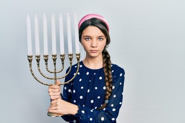 Sticker - Young brunette girl holding menorah hanukkah jewish candle skeptic and nervous, frowning upset because of problem. negative person.