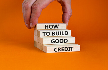 Wall Mural - Symbol of building success foundation and good credit symbol. Wooden blocks with words how to build good credit. Beautiful orange background. Businessman hand. Business and build good credit concept.