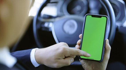 Man hand using chromakey mobile phone with empty green screen in modern car. Mockup touchscreen. Internet searching. Scrolling smartphone display closeup