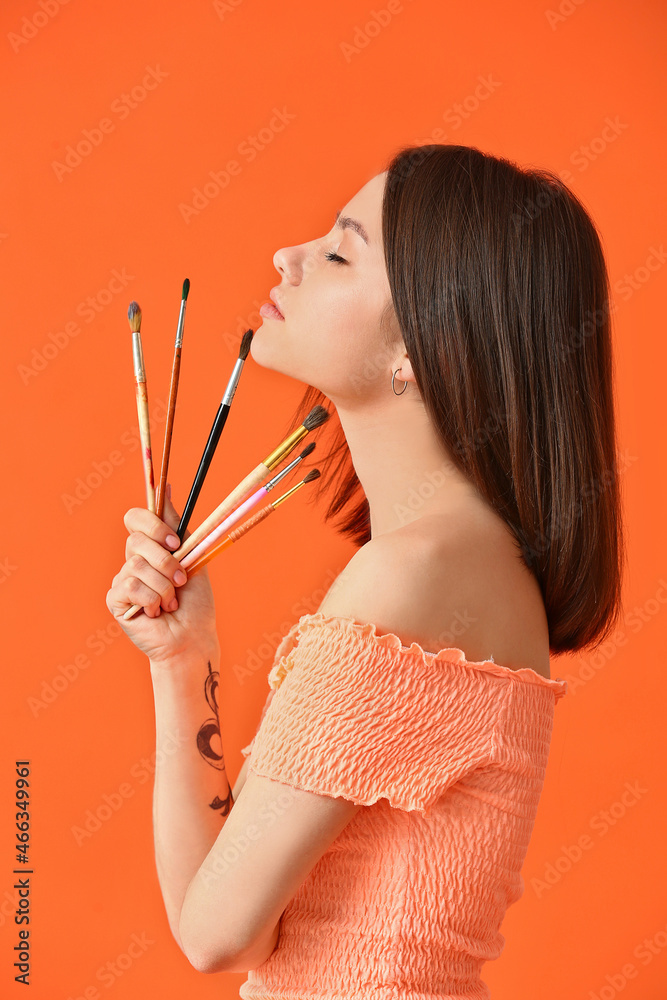 Young female artist with brushes on color background