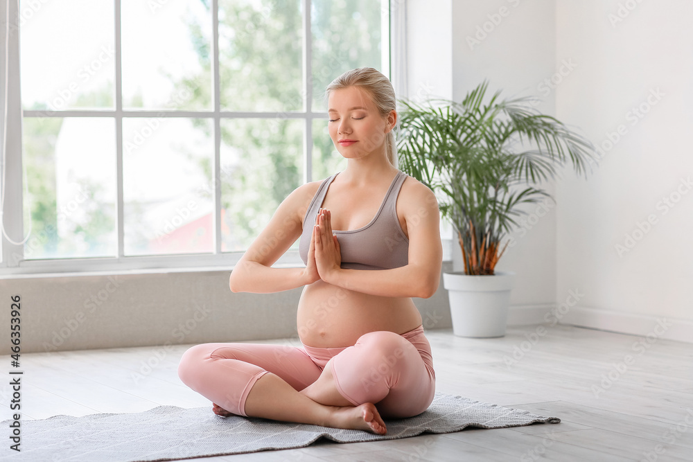 Young pregnant woman meditating indoors