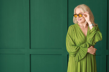 Wall Mural - Beautiful mature woman in sunglasses on green background
