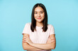 © Mix and Match Studio - Smiling asian girl in t-shirt, holding arms crossed, ready for action pose, standing over blue background