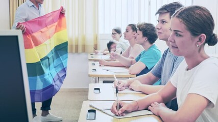 Wall Mural - Pupils sitting in class and listening carefully to male teacher. He holding LGBT pride flag in hands and talking about sex minorities. High quality 4k footage