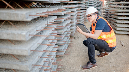 Wall Mural - Smart Asian worker man or male civil engineer with protective safety helmet and reflective vest using digital tablet for project planning and checking material at construction site.