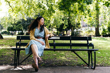 Young Woman With Eyes Closed Sitting On Bench In Park