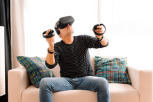 Mature Man Wearing Virtual Reality Simulator Holding Remote Control While Sitting On Sofa