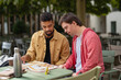 © Halfpoint - Young man with Down syndrome with his mentoring friend sitting outdoors in cafe and studying.