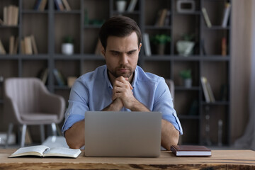 Poster - Pensive young businessman employee manager looking at laptop screen, considering difficult problem solution, thinking on online project, enjoying distant freelance workday in modern home office.