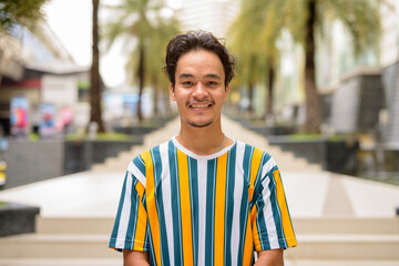 Wall Mural - Portrait of handsome multi-ethnic young man wearing colorful shirt outdoors during summer and smiling