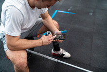 Sportsman using smart phone having energy drink while sitting on barbell in gym