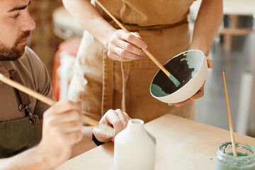 Wall Mural - Close up of two young artists decorating ceramics in pottery workshop, copy space