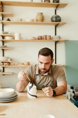 Wall Mural - Warm toned portrait of creative bearded man decorating ceramics in pottery workshop, copy space