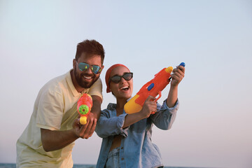 Sticker - Happy couple with water guns against light blue sky at sunset