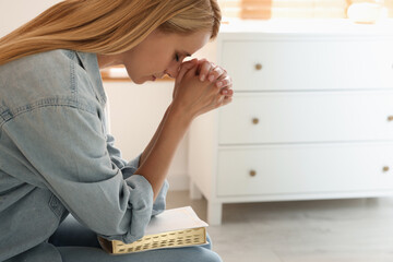 Wall Mural - Religious young woman with Bible praying indoors. Space for text