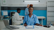 © DC Studio - Close up of woman working as nurse sitting at desk and reading documents, files, papers of patient checkup. Person wearing uniform and stethoscope in healthcare cabinet at facility