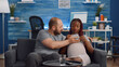 © DC Studio - Interracial couple with pregnancy watching movie on TV while eating popcorn. Multi ethnic parents expecting baby and sitting on living room couch. Mixed race people relaxing with television