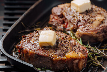 Wall Mural - cooking sumptuous steaks in a grill pan with butter spreading over the steak seasoned with ground pepper and salt with rosemary sprigs