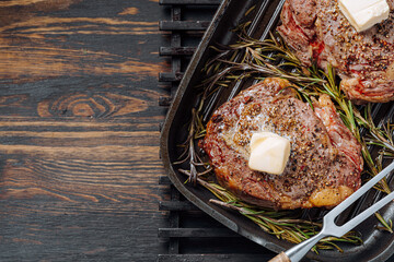 Wall Mural - cooking sumptuous steaks in a grill pan with butter spreading over the steak seasoned with ground pepper and salt with rosemary sprigs