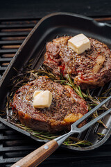 Wall Mural - cooking sumptuous steaks in a grill pan with butter spreading over the steak seasoned with ground pepper and salt with rosemary sprigs