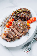 Wall Mural - juicy well-fried ribeye steaks on a white platter on a white marble surface with raspmarine and fried cherry tomatoes and peppers. steaks are sliced and ready to serve