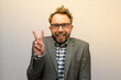 Funny nerdy weirdo caucasian bearded man with eyeglasses in a suit posing with peace sign for a photo 