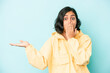 © Asier - Young latin woman isolated on blue background impressed holding copy space on palm.