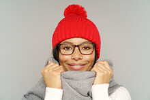 Studio Portrait Of Cheerful African American Female Wearing Knitted Red Hat And Scarf Preparing For Winter Frost And Cold. Happy Smiling Black Female In Eyeglasses In Warm Accessories Over Gray Wall