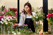 young caucasian female arranging blossom flowers making bouquet in small shop. business, craft and hand made concept. nice experienced professional florist is concentrated on working.