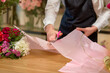 florist woman cutting envelope for bouquet decoration using scissors, in shop. cropped female in apron concentrated on work, carefully neatly making bouquet for clients, customers.