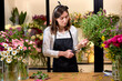 Photo of successful modern florist wearing apron making creating bouquet of blooming colorful different flowers in modern interior floral shop, using scissors. small flower shop business concept