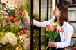 Side view on young attractive nice woman taking one flower to add it on bouquet. Caucasian lady florist in apron making decorating bouquet of fresh flowers in shop, at work place. indoors.