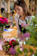 professional florist woman made bouquet of seasonal blooming flowers, preparing them for sale. Charming caucasian lady in apron at work place, focused and concentrated. in modern small flower shop