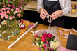 Female florist at work arranging various flowers in bouquet, decorating bouquet. close-up hands of young woman standing behind desk making bouquet of fresh flowers. focus on hands. beauty