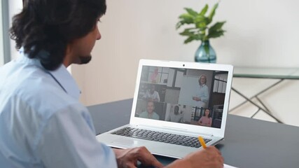 Wall Mural - Focused indian man using laptop computer for studying online, watching webinar, take a part in educational course, takes notes, writing down, group of diverse people involved in meeting on the screen